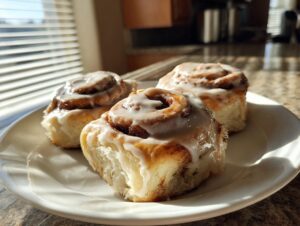Three fluffy gluten-free cinnamon rolls generously topped with white icing, sitting on a white plate.