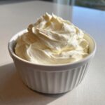 A small white ramekin filled with freshly whipped, creamy homemade mayonnaise, showing soft peaks.