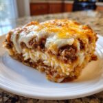 A close-up slice of french onion ground beef and rice casserole topped with melted white and cheddar cheese.