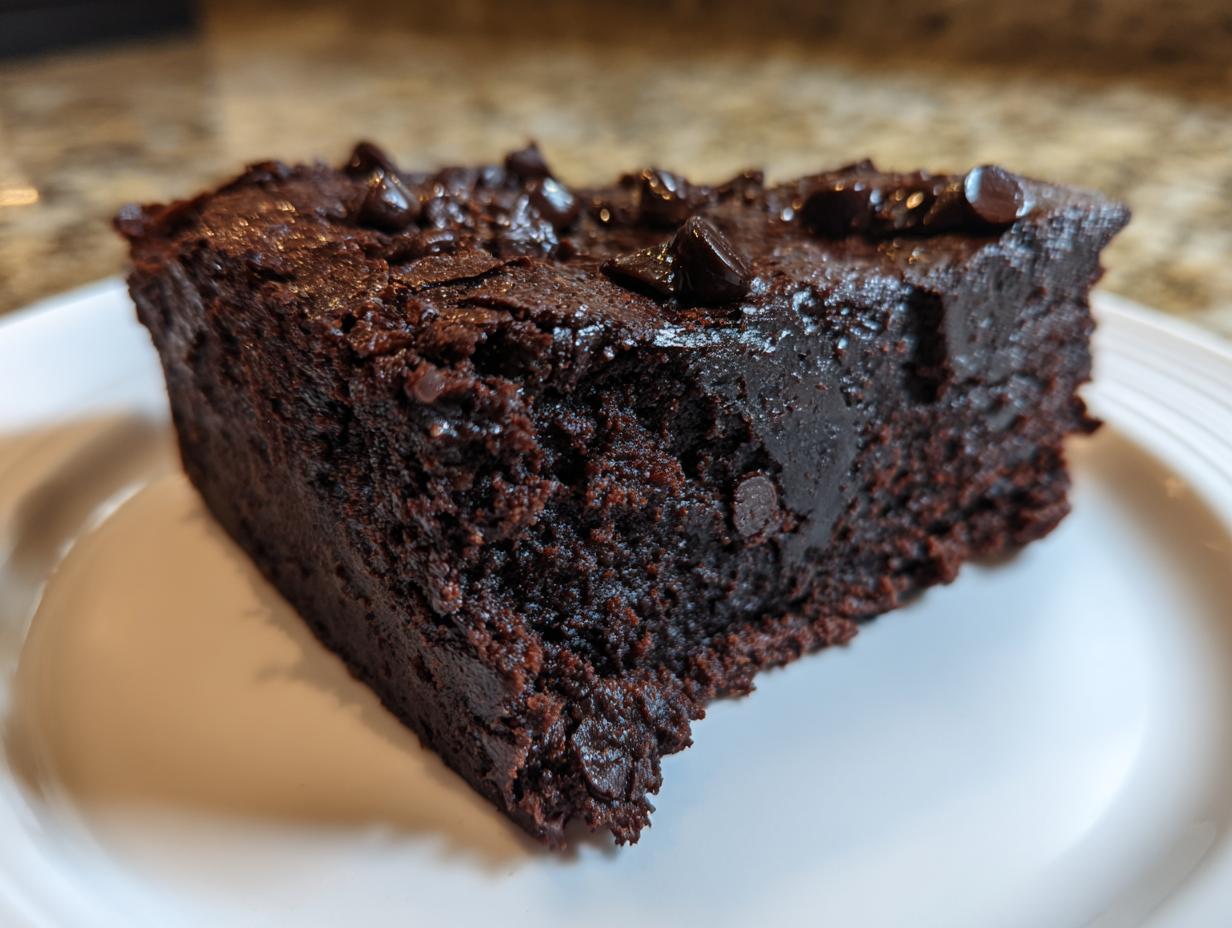 Close-up of a rich, dark slice of brownie made from black bean brownie batter, topped with chocolate chips.