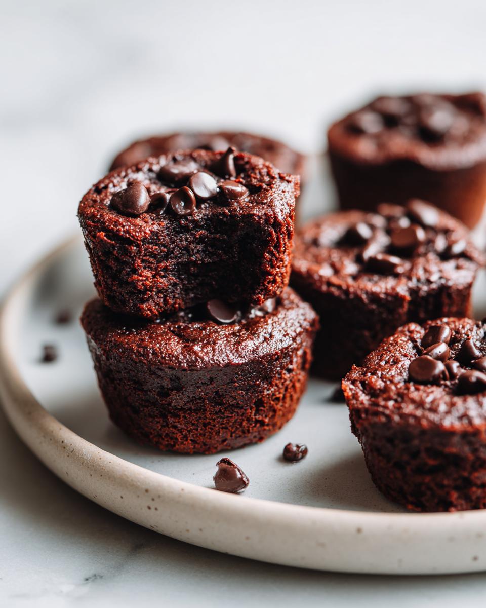 A stack of fudgy black bean brownie bites topped with chocolate chips, with more bites blurred in the background.