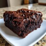 A rich, fudgy square of a baked black bean brownie, topped with melted chocolate chips, served on a white plate.