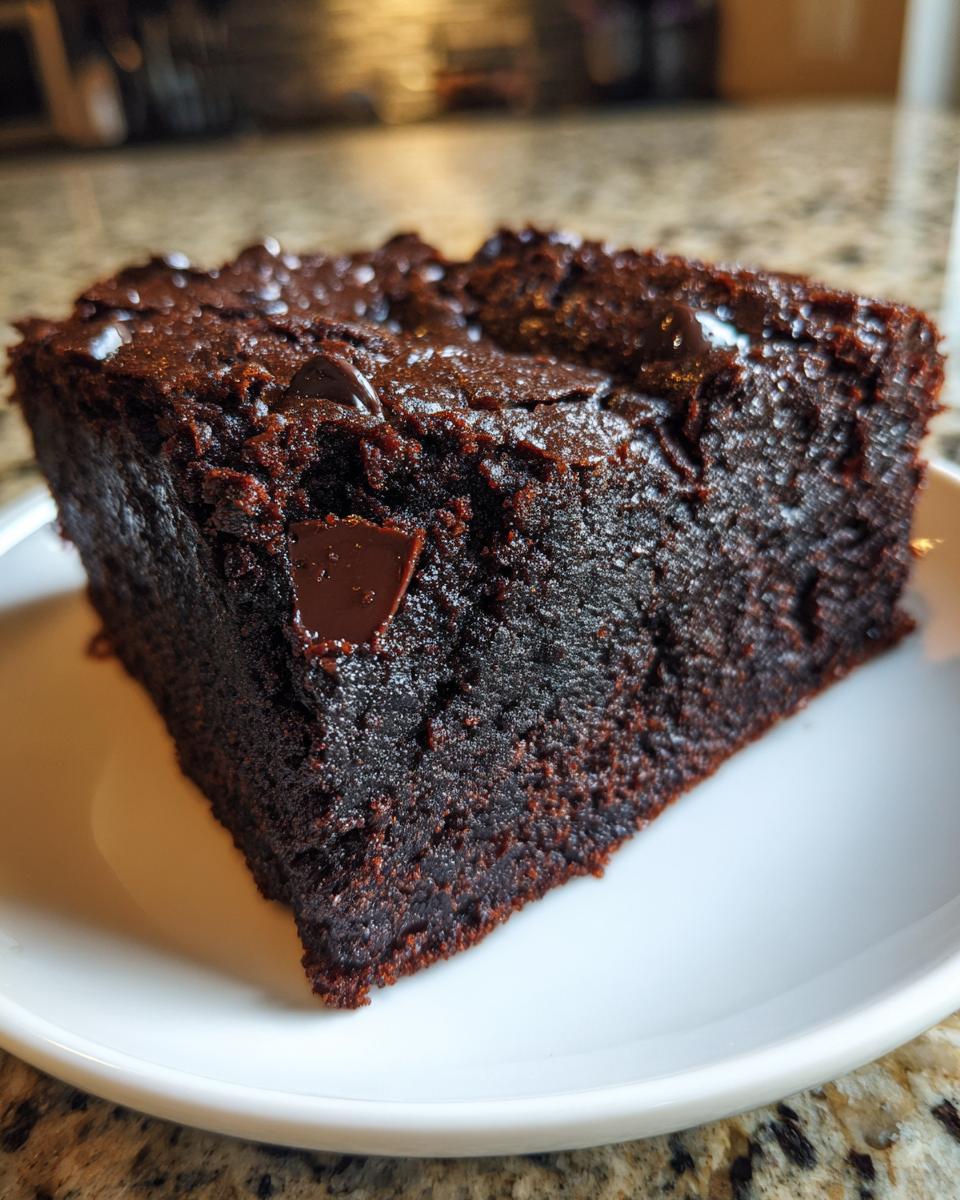 Close-up of a fudgy, dark chocolate brownie slice, likely made from black bean brownie batter, topped with melted chips.