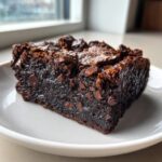 Close-up of a rich, fudgy slice of black bean brownies topped with chocolate chips on a white plate.