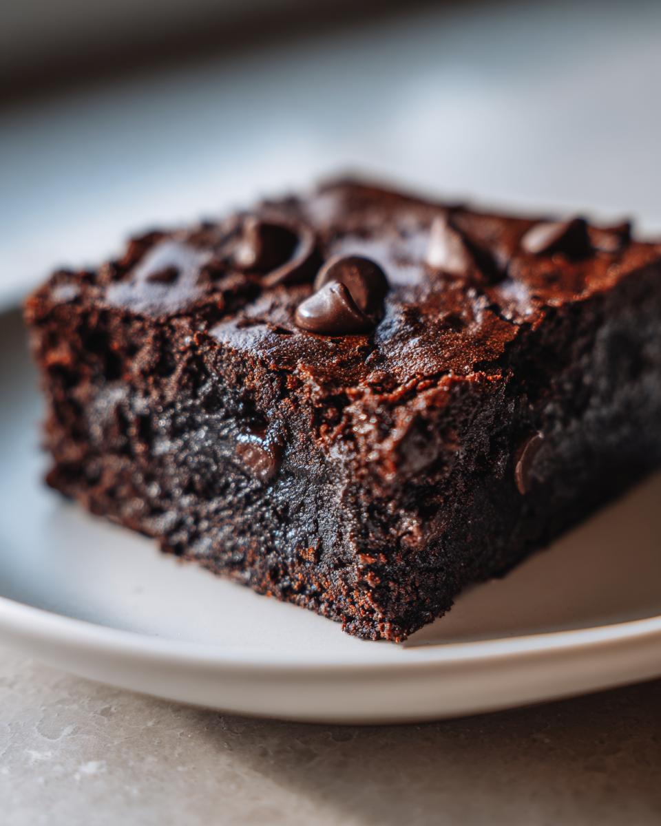 Close-up of a rich, fudgy brownie square topped with chocolate chips, likely made from black bean brownie batter.