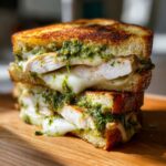 Close-up of a stacked grilled chicken pesto sandwich with melted white cheese oozing out between toasted bread slices.