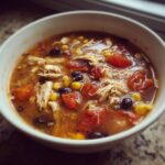 Close-up of a white bowl filled with rich chicken taco soup, featuring shredded chicken, black beans, corn, and diced tomatoes.