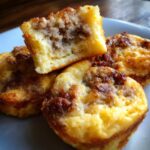A close-up of golden brown high-protein pancake sausage mini muffins, with one muffin cut open showing the savory sausage filling.
