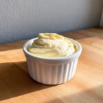 A small white ramekin filled with thick, pale yellow homemade mayonnaise olive oil, sitting on a wooden surface.