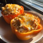 Two bright orange bell peppers filled with shredded keto buffalo chicken and topped with melted cheddar and mozzarella cheese.
