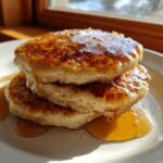 A close-up of a stack of three fluffy maple ginger pancakes generously drizzled with golden syrup.
