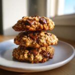 Three freshly baked oatmeal peanut butter chocolate chip cookies stacked on a white plate.