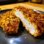 Close-up of parmesan crusted chicken cut in half showing juicy white meat inside the golden, crispy crust.