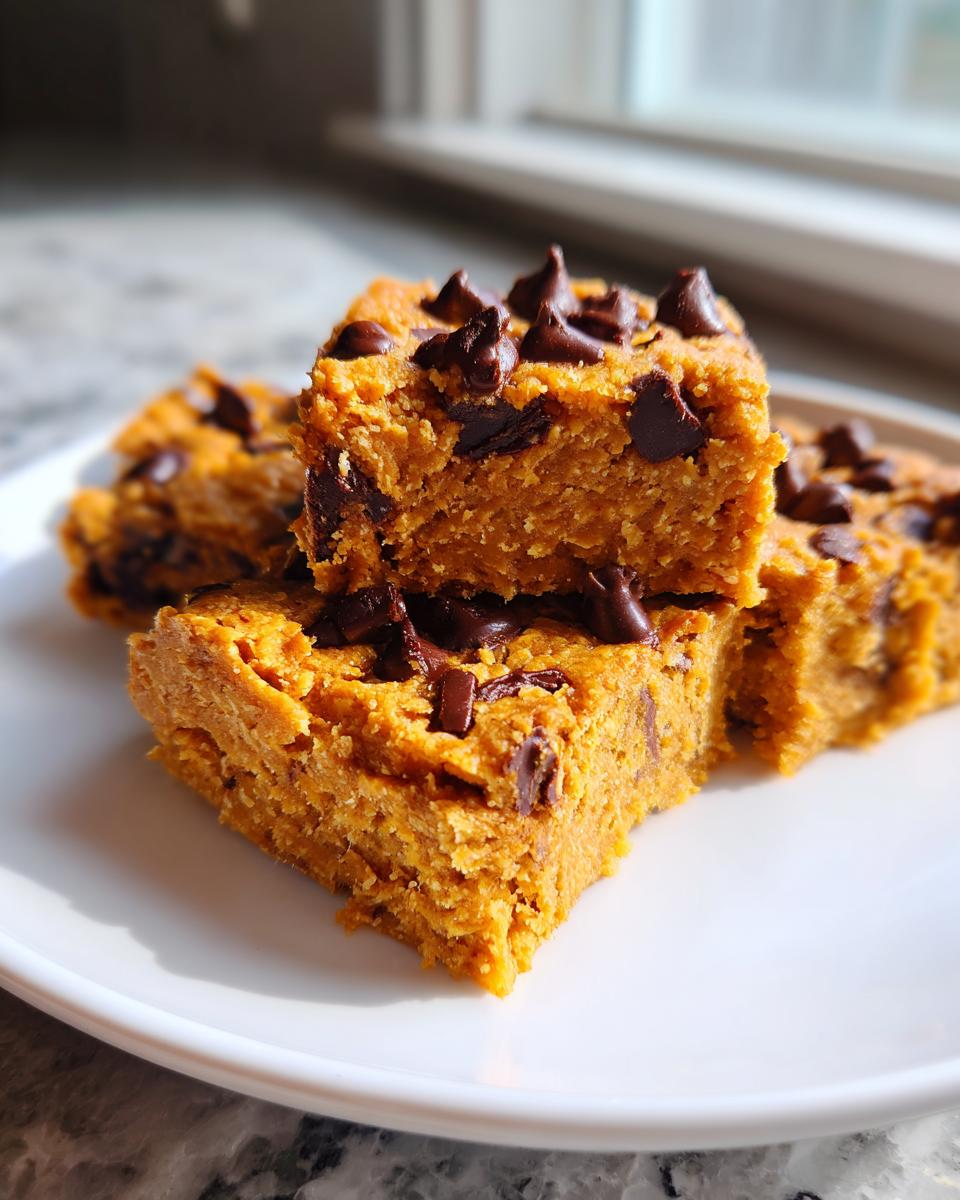 A stack of rich, orange-hued peanut butter chocolate chip cookie bars topped with melted chocolate chips on a white plate.