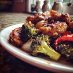 Close-up of glazed chicken pieces mixed with roasted broccoli, onions, and cashews from the sheet pan cashew chicken recipe.