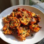 A pile of golden brown, crispy smashed carrot bites topped with visible herbs and melted cheese on a white plate.