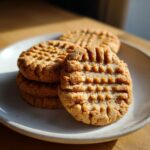 Close-up of a stack of softest peanut butter cookies featuring classic crisscross fork marks on a light plate.