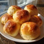 A plate piled high with freshly baked, golden-brown sourdough discard dinner rolls, glistening under natural light.