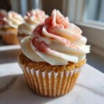 A close-up of one of the strawberry cheesecake cupcakes featuring a graham cracker crust base and swirled cream cheese frosting with strawberry dust.