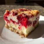 A close-up slice of strawberry cheesecake dump cake showing layers of crust, creamy filling, and bright red strawberry topping.