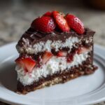 A decadent slice of strawberry chocolate shell cake featuring dark layers, white cream, and fresh strawberries on top.