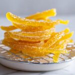 A pile of bright yellow, sugar-coated candied lemon peel strips resting on a small wire cooling rack.