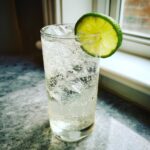 A tall glass filled with ice and a bubbly vanilla vodka soda, garnished with a bright lime wheel.