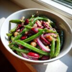 Close-up of a vibrant three bean salad featuring green beans, kidney beans, and chickpeas with red onion slices.