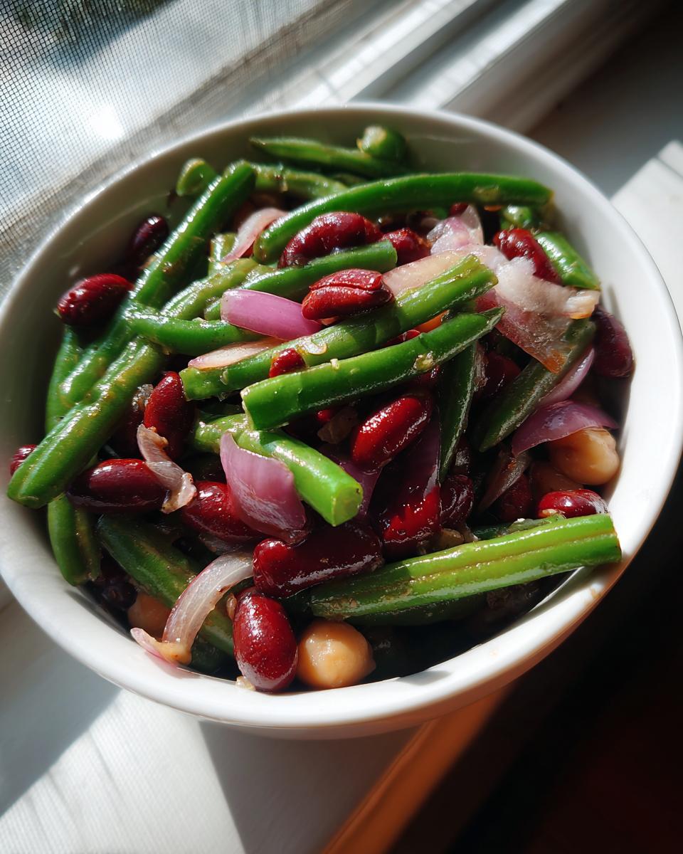Close-up of a fresh three bean salad featuring green beans, kidney beans, and chickpeas with red onion slices.
