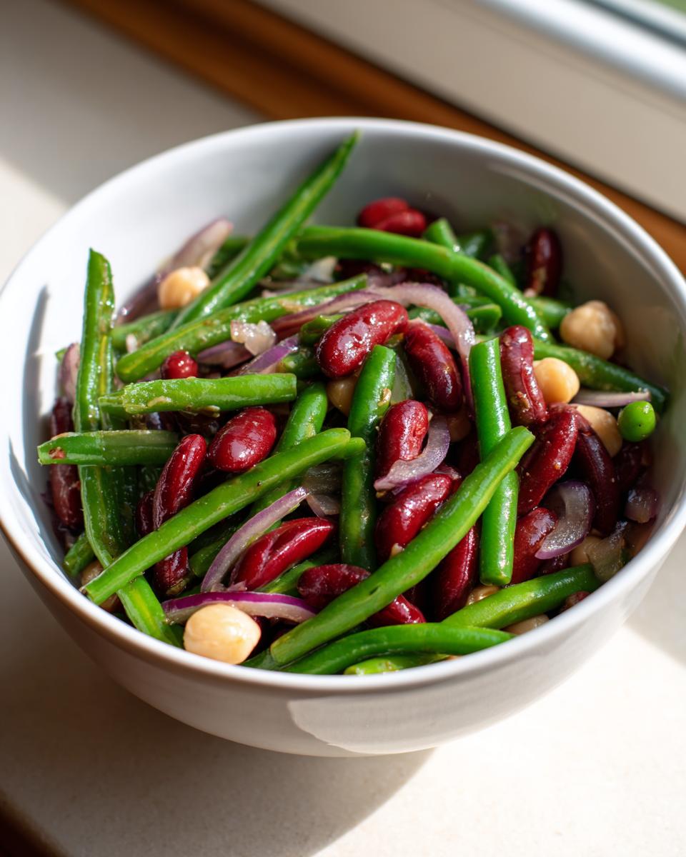 Close-up of a vibrant three bean salad featuring green beans, kidney beans, and chickpeas with sliced red onion.