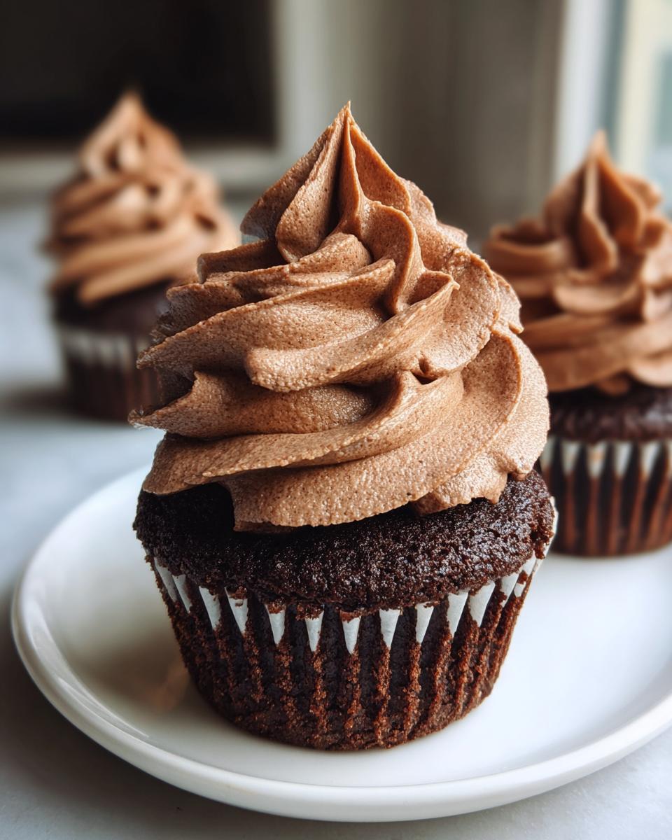 A close-up of a rich chocolate cupcake topped with perfectly piped whipped chocolate ganache cupcakes frosting.