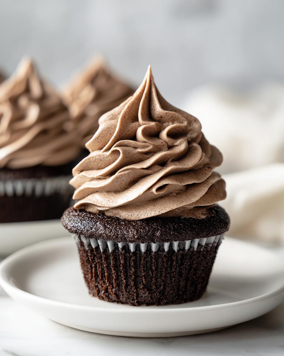 A single dark chocolate cupcake topped with a tall swirl of light brown whipped chocolate ganache.
