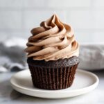 A single dark chocolate cupcake topped high with light brown whipped chocolate ganache frosting.