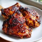 Three pieces of perfectly cooked, deeply glazed marinated chicken thighs resting on a light plate.