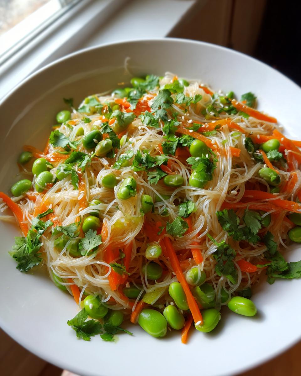 Close-up of a bowl filled with asian edamame salad featuring clear glass noodles, bright green edamame, shredded carrots, and fresh cilantro.