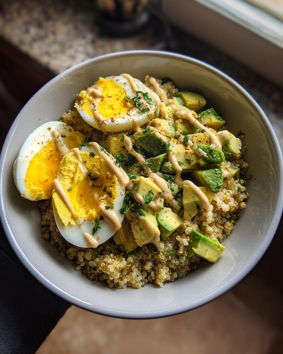 A close-up overhead view of a healthy avocado egg quinoa bowl topped with a creamy sauce and spices.