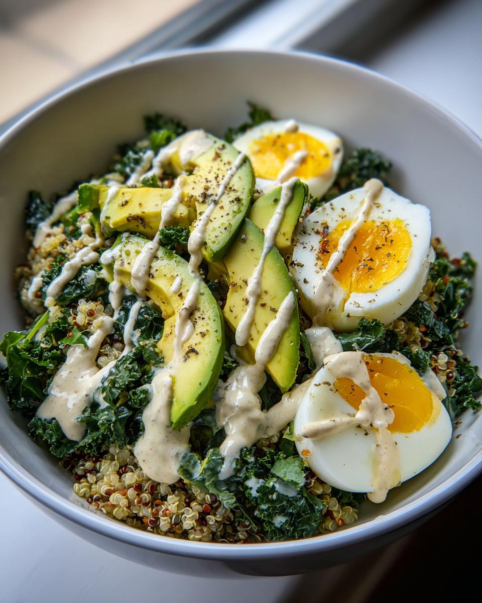 A vibrant avocado egg quinoa bowl featuring sliced avocado, halved soft-boiled eggs, kale, and a creamy tahini dressing.