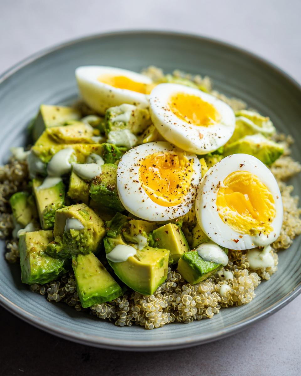 Close-up of an avocado egg quinoa bowl featuring diced avocado, quinoa, and halved soft-boiled eggs seasoned with pepper.