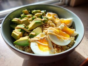 A vibrant avocado egg quinoa bowl featuring sliced avocado, soft-boiled egg wedges, and a creamy orange drizzle.
