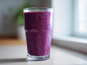 A tall glass filled with a thick, vibrant purple blueberry yogurt smoothie, condensation visible on the glass.