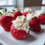 Several bright red cheesecake stuffed strawberries topped generously with fluffy white whipped cream, served on a white plate.