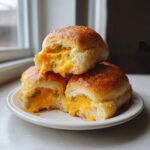 Close-up of cheesy crescent rolls stacked on a white plate, showing gooey cheddar cheese and green onions filling.