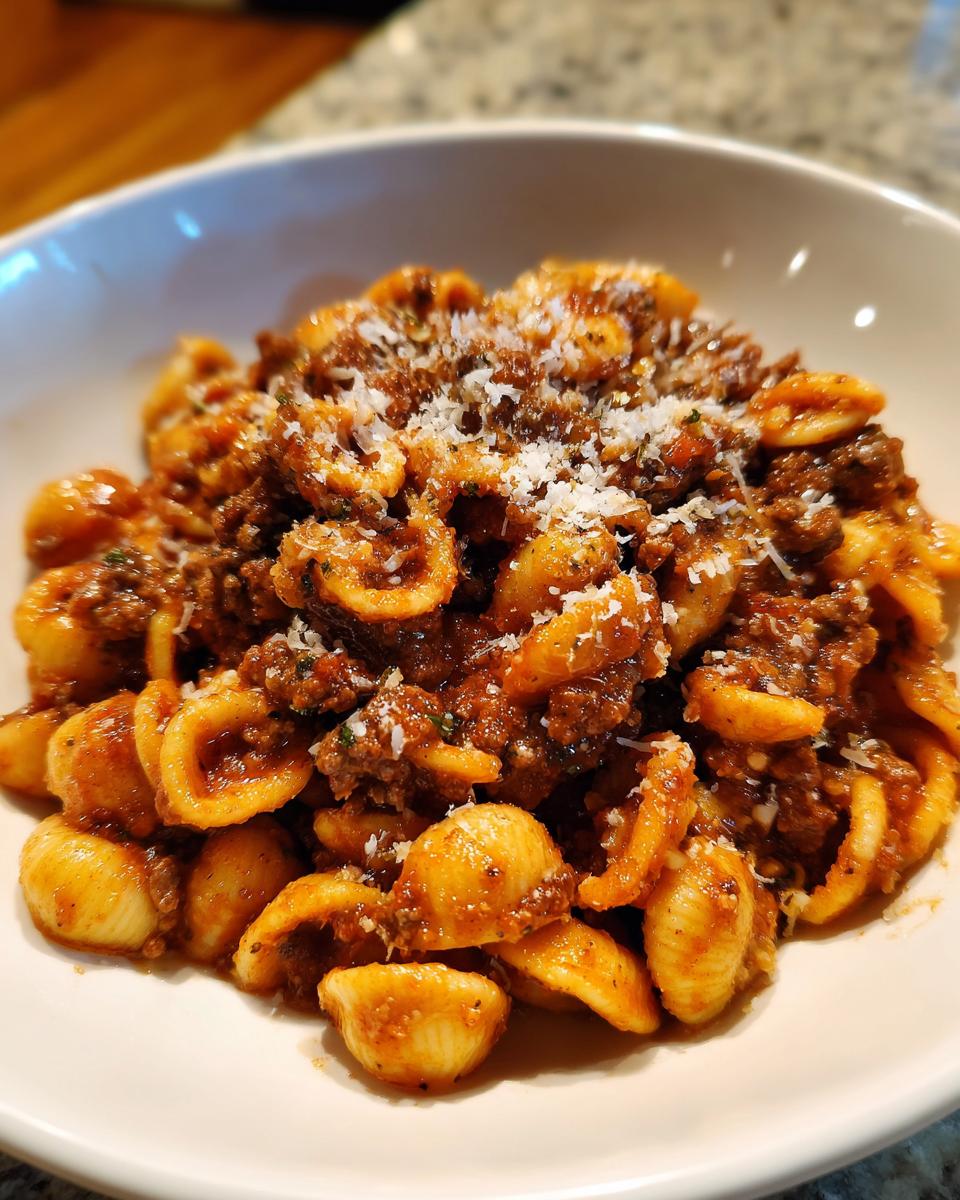 Close-up of a white bowl filled with rich ground beef orecchiette pasta topped with grated Parmesan cheese.