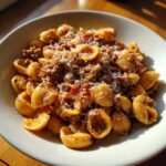 A close-up, sunlit bowl of ground beef orecchiette pasta topped generously with grated Parmesan cheese.