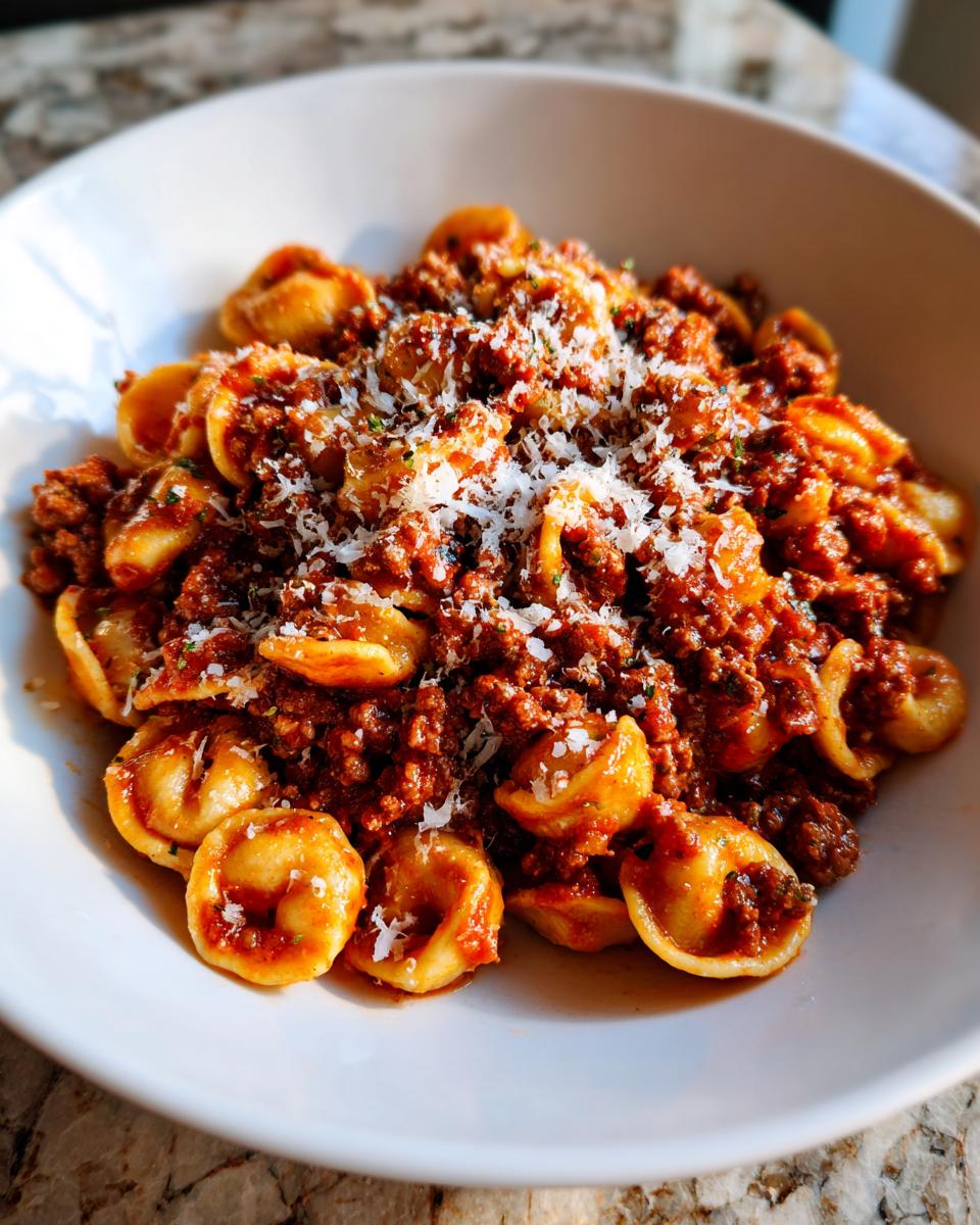 Close-up of a bowl of ground beef orecchiette pasta topped generously with grated Parmesan cheese.